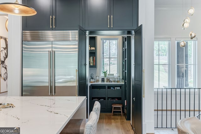 kitchen with hardwood / wood-style flooring, light stone countertops, stainless steel built in refrigerator, and pendant lighting