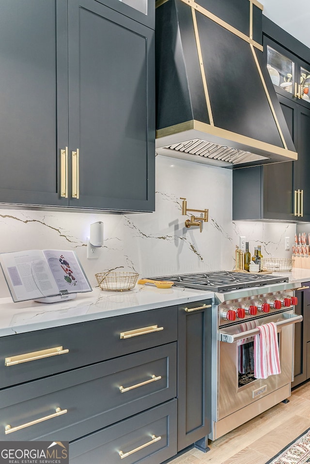 kitchen with light stone countertops, wall chimney exhaust hood, luxury range, light hardwood / wood-style flooring, and decorative backsplash