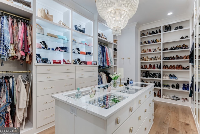 spacious closet with light wood-type flooring and an inviting chandelier