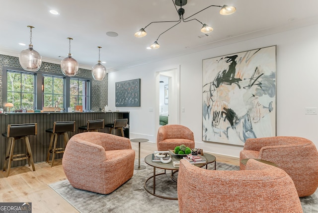 living room featuring crown molding, light wood-type flooring, a notable chandelier, and indoor bar