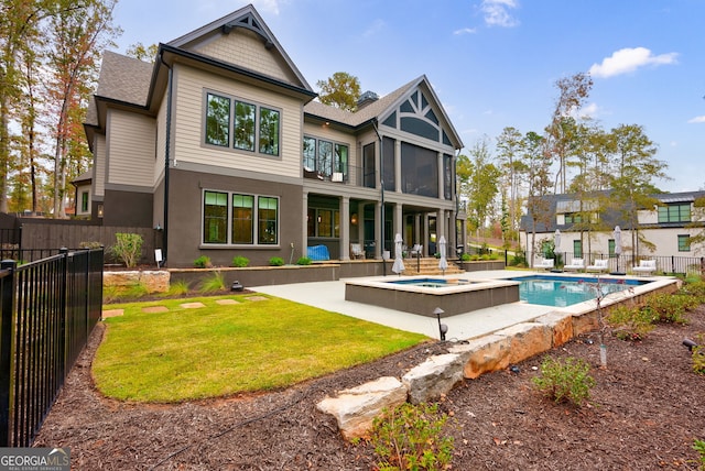 rear view of property with a lawn, a sunroom, a patio, and a swimming pool with hot tub