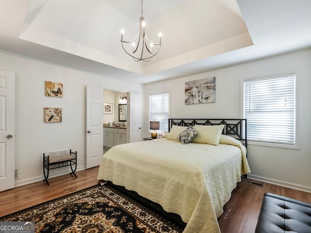 bedroom with a raised ceiling, connected bathroom, and dark hardwood / wood-style flooring