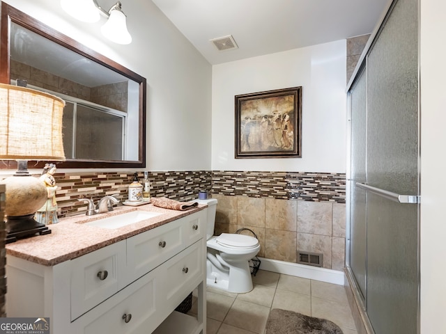 bathroom with tile patterned floors, vanity, a shower with door, tile walls, and toilet