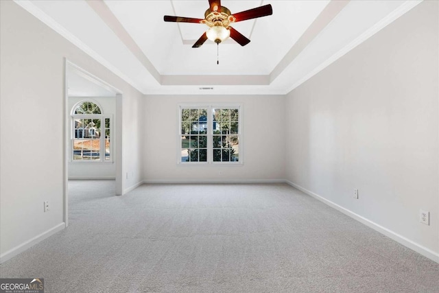 carpeted empty room with a tray ceiling, ceiling fan, plenty of natural light, and ornamental molding