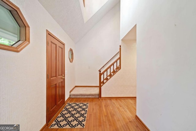 entrance foyer with a textured ceiling, light hardwood / wood-style flooring, and lofted ceiling