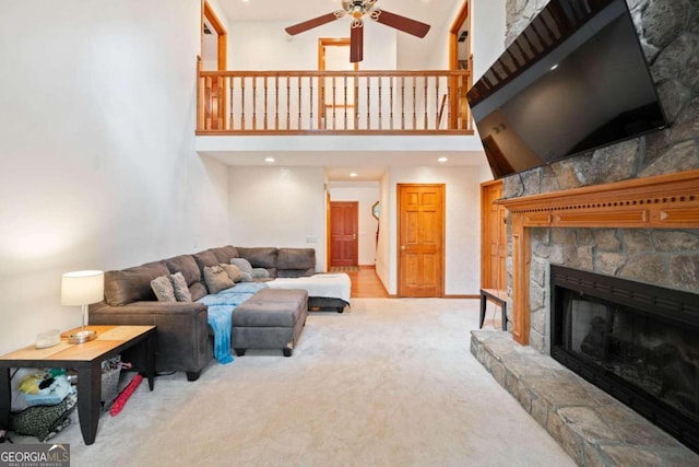 living room featuring a high ceiling, a stone fireplace, light carpet, and ceiling fan