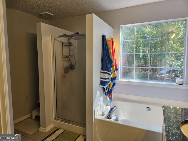 bathroom with a textured ceiling, tile patterned floors, a healthy amount of sunlight, and separate shower and tub