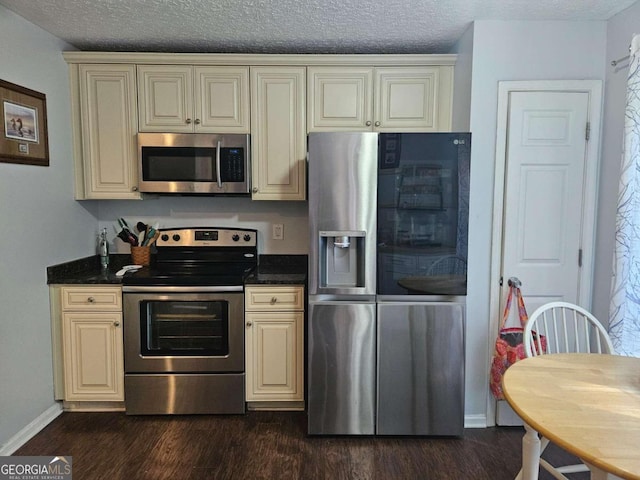 kitchen with appliances with stainless steel finishes, cream cabinets, a textured ceiling, and dark hardwood / wood-style flooring