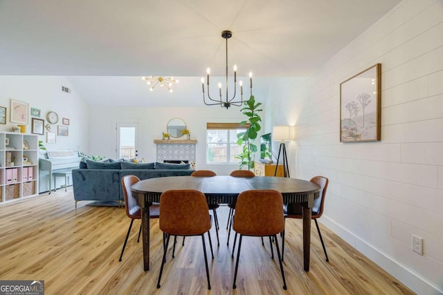 dining area with a tile fireplace, light wood-type flooring, lofted ceiling, and a notable chandelier