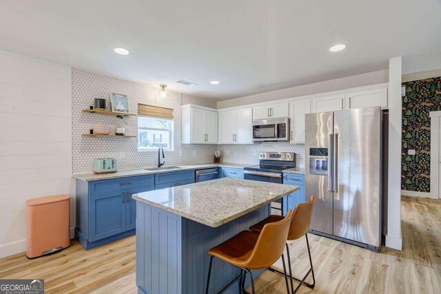 kitchen featuring light wood-type flooring, appliances with stainless steel finishes, sink, white cabinets, and a center island