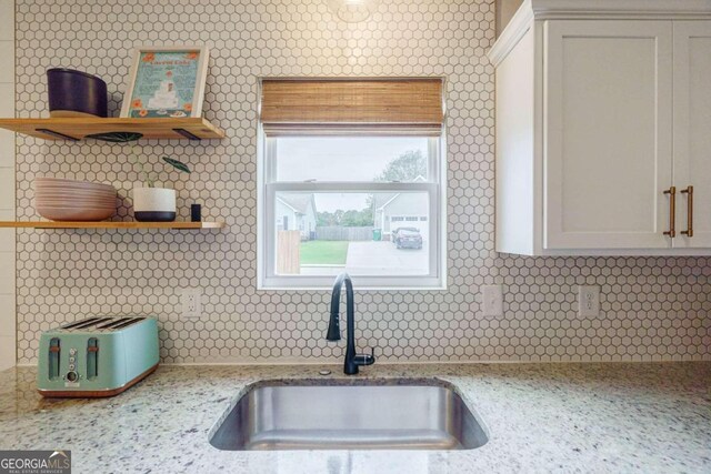 kitchen featuring white cabinetry, sink, light stone counters, and tasteful backsplash