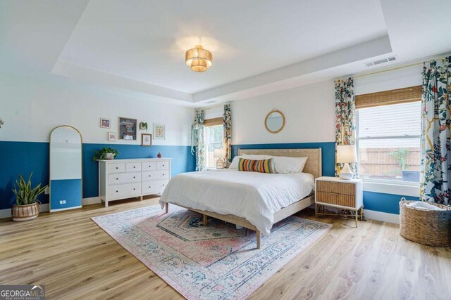 bedroom featuring light hardwood / wood-style floors, multiple windows, and a tray ceiling