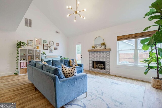 living room featuring high vaulted ceiling, light hardwood / wood-style flooring, a tile fireplace, and an inviting chandelier