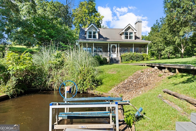 exterior space featuring a sunroom, a lawn, and a water view