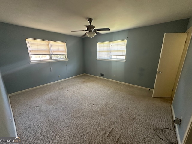 carpeted spare room featuring a wealth of natural light and ceiling fan