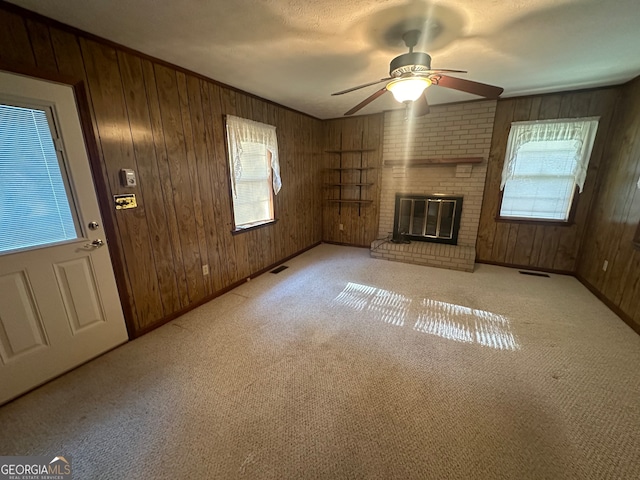 unfurnished living room with wood walls, a wealth of natural light, ceiling fan, and a fireplace