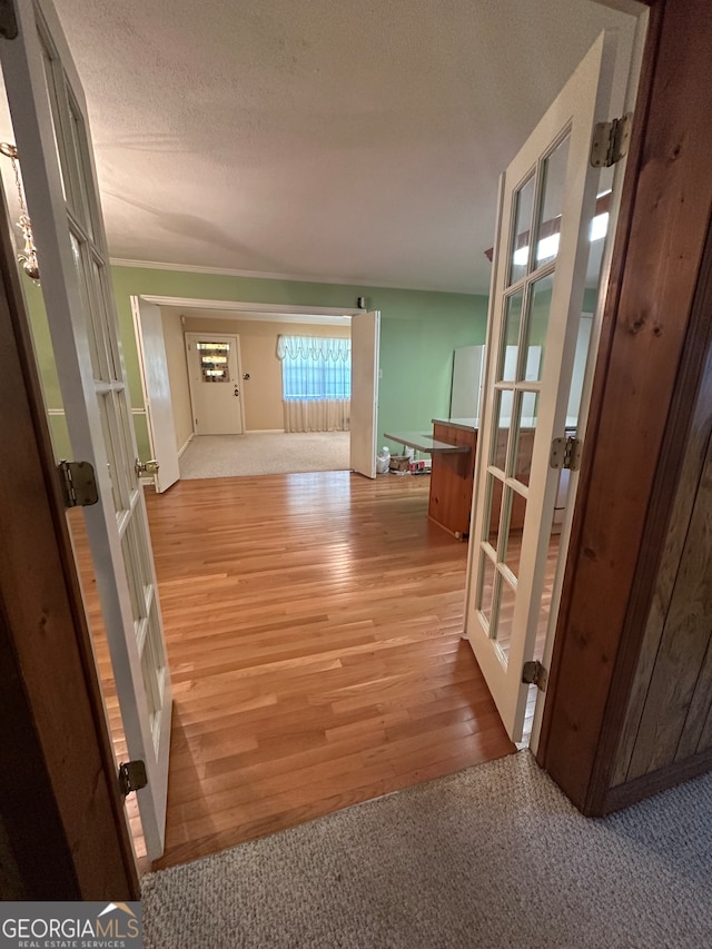 corridor with light wood-type flooring, french doors, and a textured ceiling