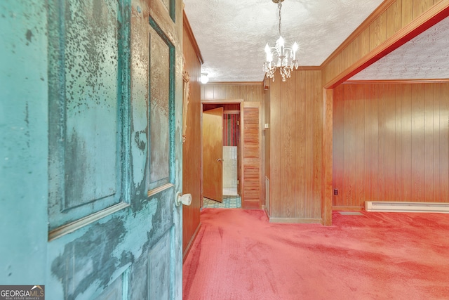 carpeted empty room with ornamental molding, baseboard heating, a textured ceiling, a chandelier, and wooden walls