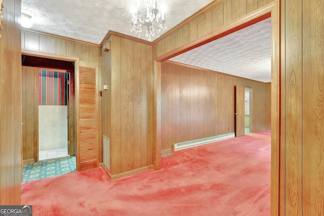 hall featuring baseboard heating, a textured ceiling, a notable chandelier, wooden walls, and carpet floors