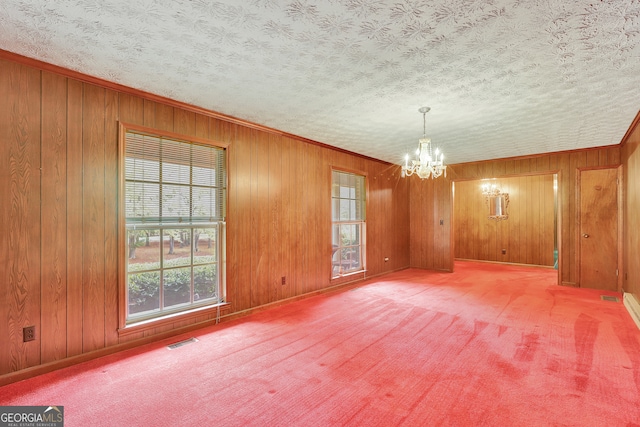 carpeted empty room featuring a textured ceiling, wooden walls, and a chandelier