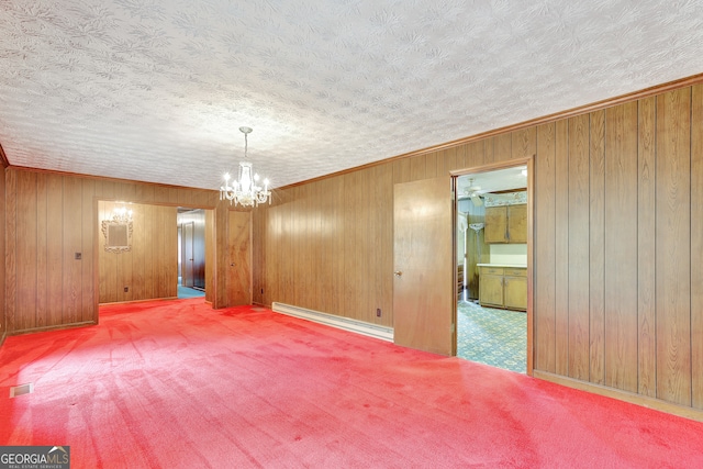 carpeted spare room with ornamental molding, a textured ceiling, a notable chandelier, wooden walls, and a baseboard heating unit