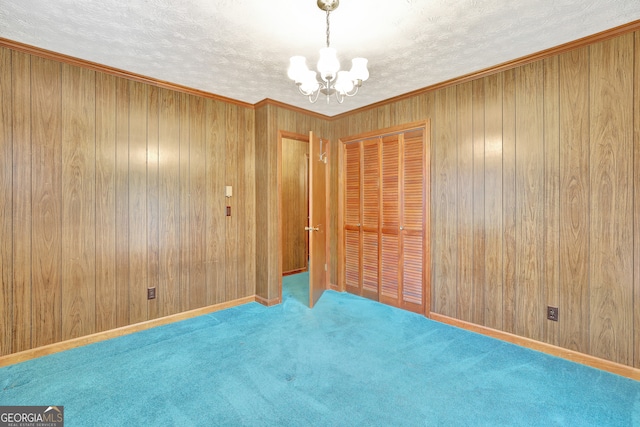 unfurnished room featuring crown molding, carpet floors, a textured ceiling, a notable chandelier, and wooden walls