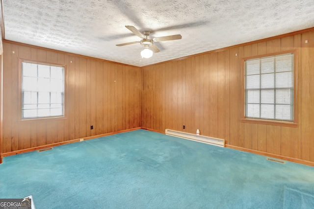 carpeted spare room featuring ornamental molding, a textured ceiling, wood walls, a baseboard radiator, and ceiling fan