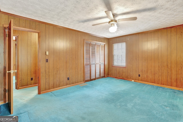 carpeted empty room featuring a textured ceiling, wooden walls, and ceiling fan