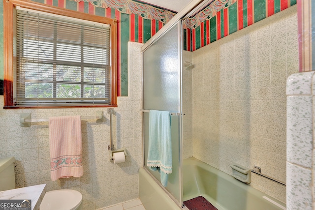 bathroom featuring tile walls, shower / bath combination with glass door, tile patterned floors, and toilet