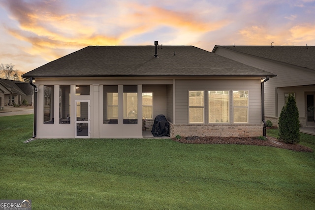 back house at dusk featuring a lawn and a patio