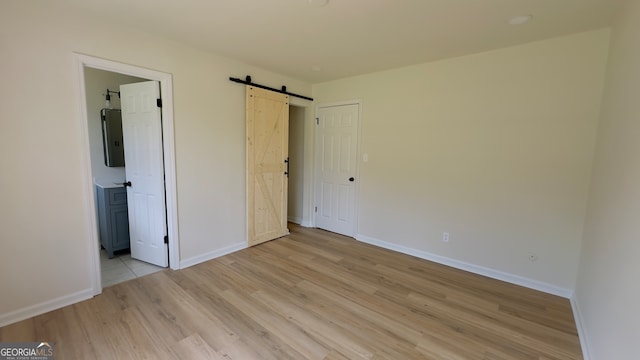 unfurnished bedroom featuring connected bathroom, electric panel, a barn door, and light hardwood / wood-style floors