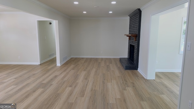 unfurnished living room featuring a brick fireplace, ornamental molding, and light hardwood / wood-style flooring