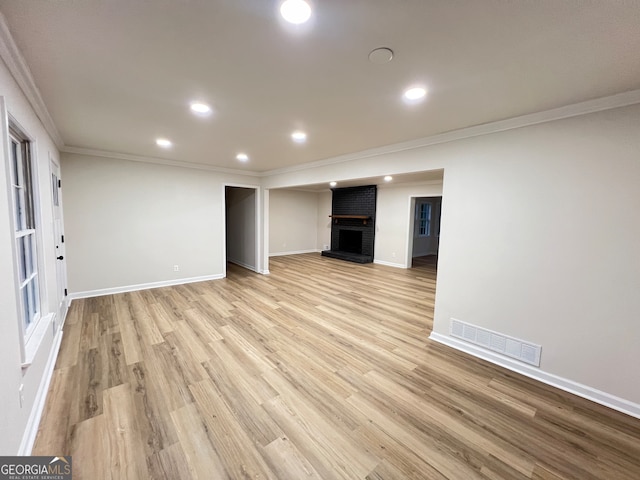 unfurnished living room featuring a brick fireplace, light wood-type flooring, and crown molding