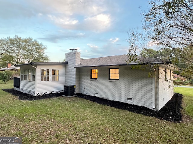 rear view of house with central AC unit and a yard