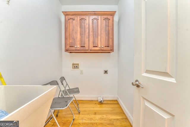 clothes washing area featuring washer hookup, electric dryer hookup, light hardwood / wood-style floors, and cabinets