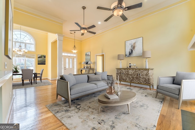 living room featuring ornamental molding, ceiling fan with notable chandelier, a towering ceiling, light hardwood / wood-style flooring, and ornate columns