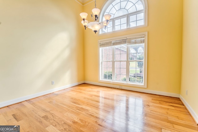 unfurnished room with a high ceiling, a chandelier, crown molding, and light hardwood / wood-style flooring