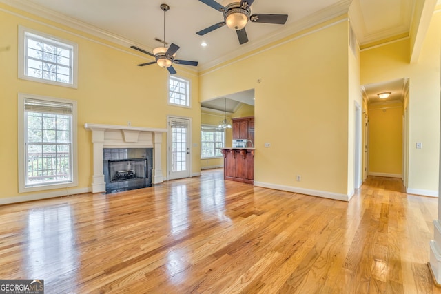 unfurnished living room with light wood-type flooring, a tiled fireplace, crown molding, and plenty of natural light