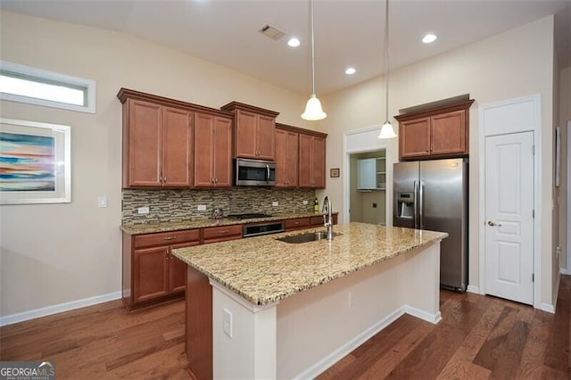 kitchen with light stone counters, a center island with sink, appliances with stainless steel finishes, dark hardwood / wood-style flooring, and pendant lighting