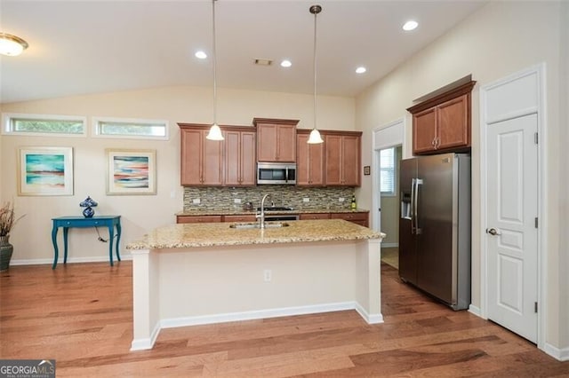 kitchen with stainless steel appliances, light hardwood / wood-style floors, a center island with sink, light stone counters, and decorative light fixtures