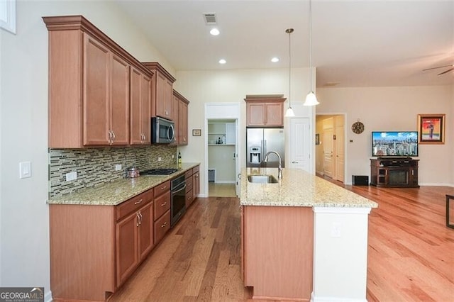 kitchen featuring stainless steel appliances, decorative light fixtures, sink, an island with sink, and light hardwood / wood-style flooring