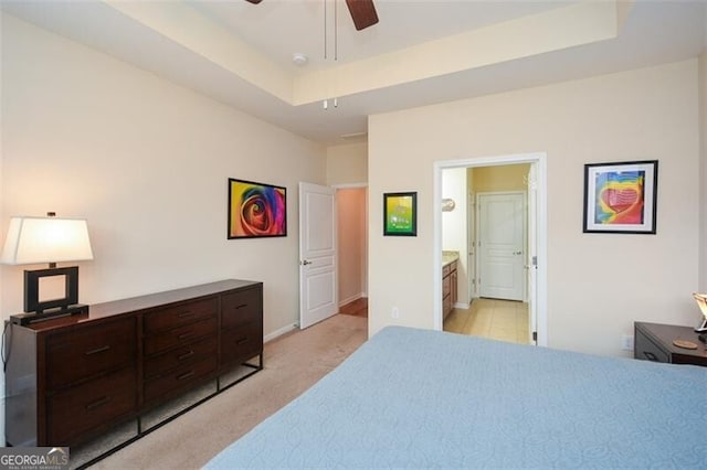 bedroom with light colored carpet, ceiling fan, a tray ceiling, and connected bathroom