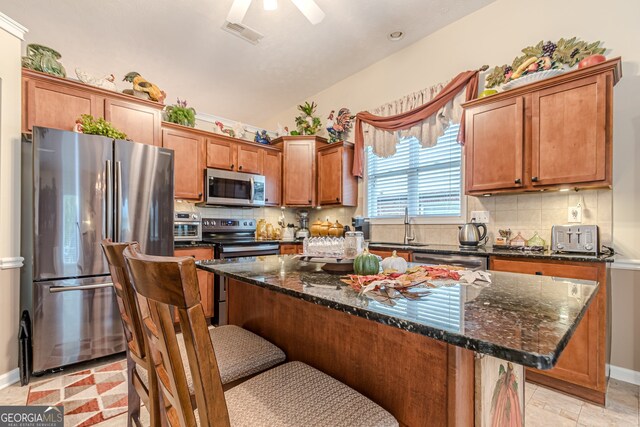 kitchen with appliances with stainless steel finishes, dark stone counters, a breakfast bar area, backsplash, and a kitchen island