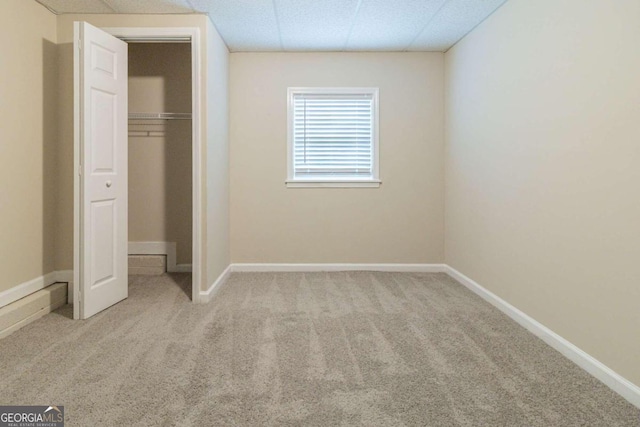 unfurnished bedroom with a closet, a drop ceiling, and light carpet