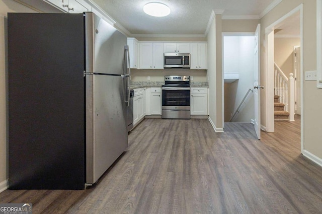 kitchen featuring white cabinets, a textured ceiling, ornamental molding, dark hardwood / wood-style floors, and appliances with stainless steel finishes