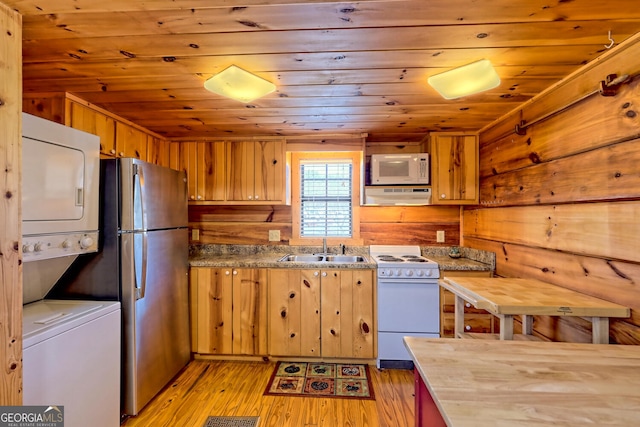 kitchen with sink, white appliances, light hardwood / wood-style flooring, range hood, and stacked washer and dryer