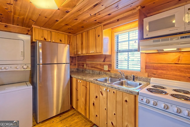 kitchen featuring stacked washer and dryer, wood walls, sink, white appliances, and light hardwood / wood-style flooring