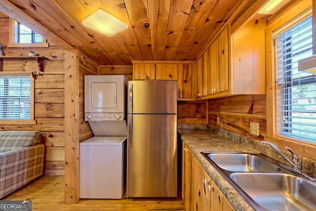 kitchen featuring wood walls, stacked washing maching and dryer, sink, and stainless steel fridge