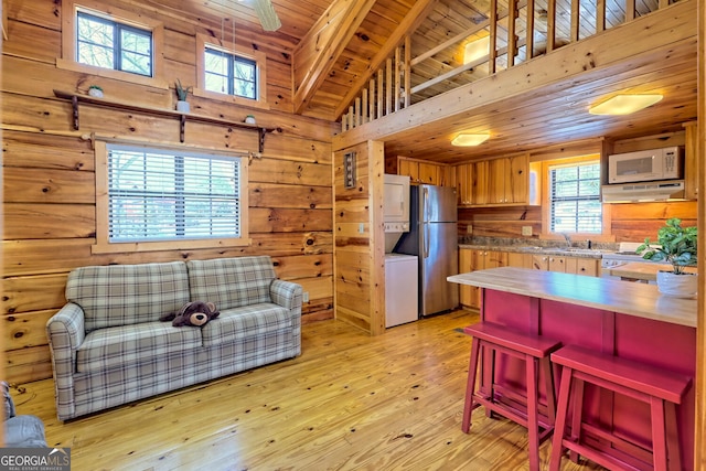 kitchen with wooden ceiling, sink, light hardwood / wood-style flooring, stainless steel fridge, and wooden walls