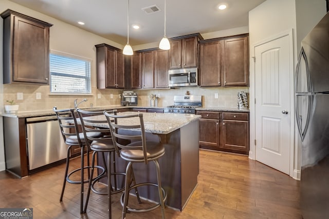 kitchen featuring stainless steel appliances, decorative light fixtures, dark brown cabinets, light stone countertops, and decorative backsplash